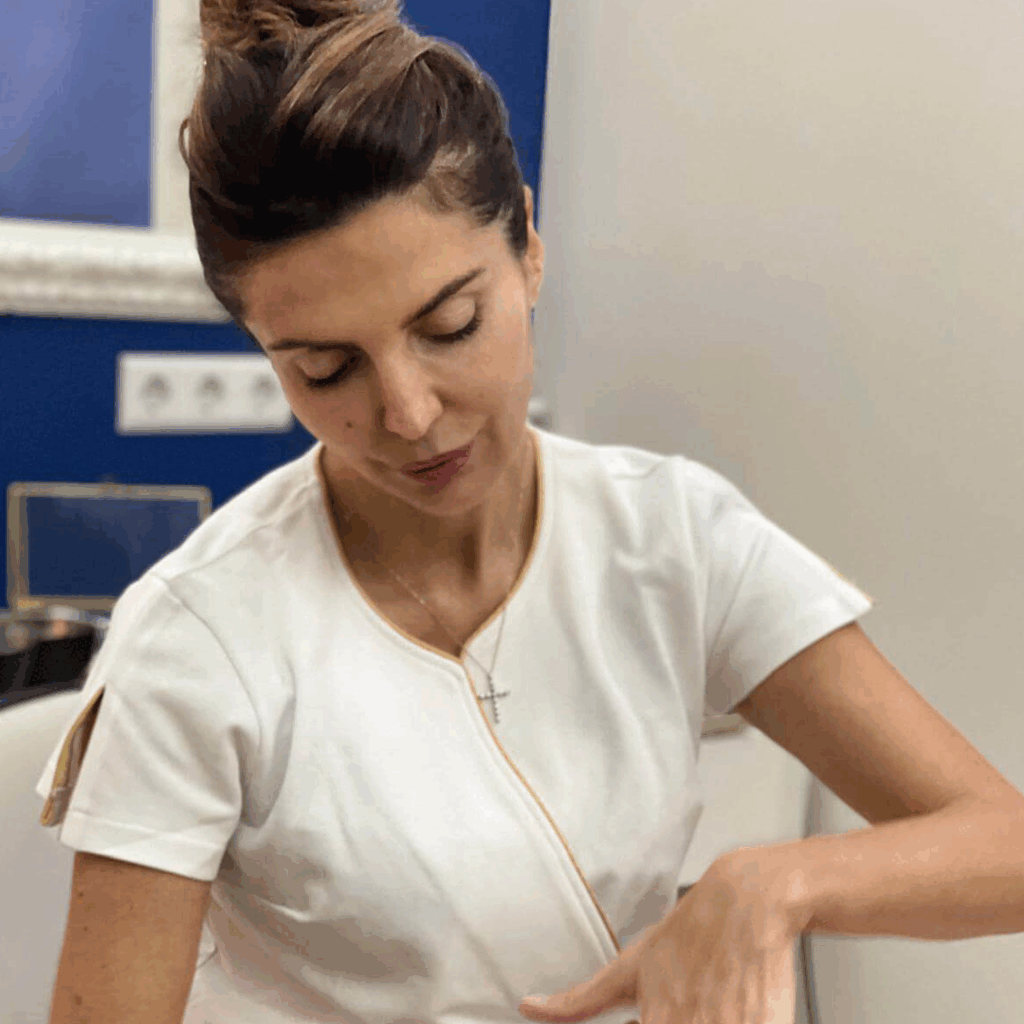 Lydia Esthetics Embassy A woman wearing a white uniform sits indoors, looking down with her hand resting on her lap—perhaps preparing for a microcurrent facial non surgical facelift or an Oxylight facial NYC treatment. New York
