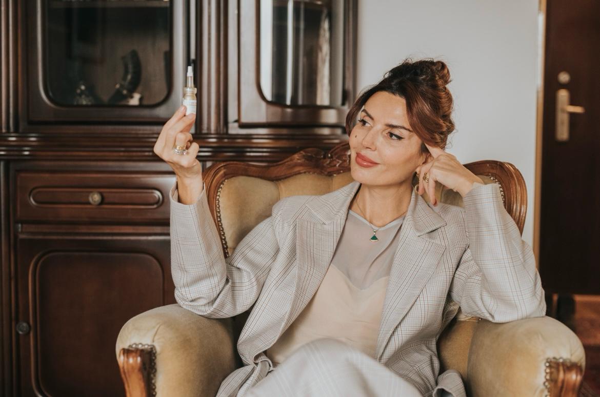 Lydia Esthetics Embassy A woman sitting in an armchair looks at a small bottle she is holding in her hand, perhaps considering microneedling with exosomes New York, with a cabinet and door in the background. New York
