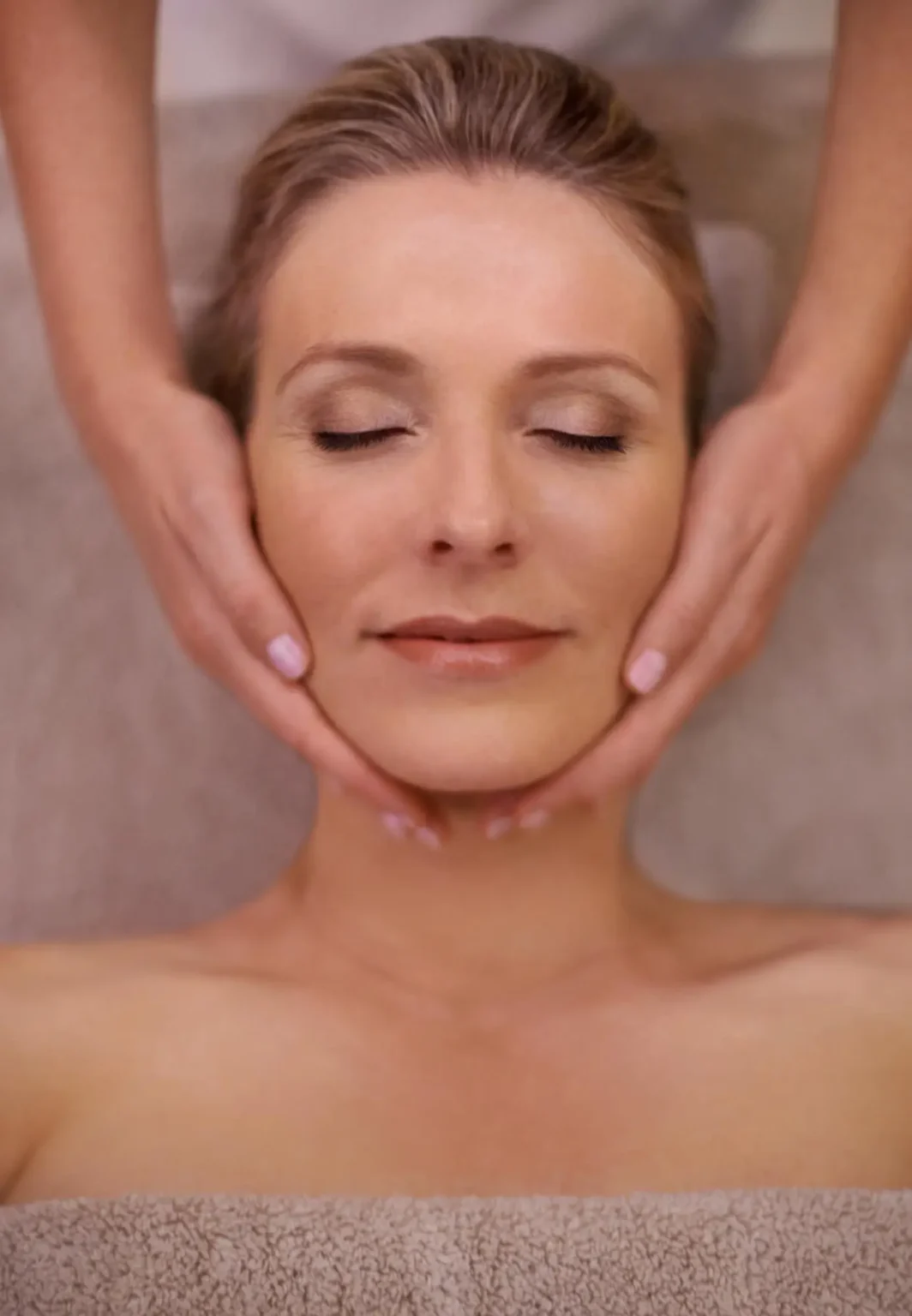 Lydia Esthetics Embassy A woman with closed eyes receives a facial massage while lying on a towel-covered surface. New York