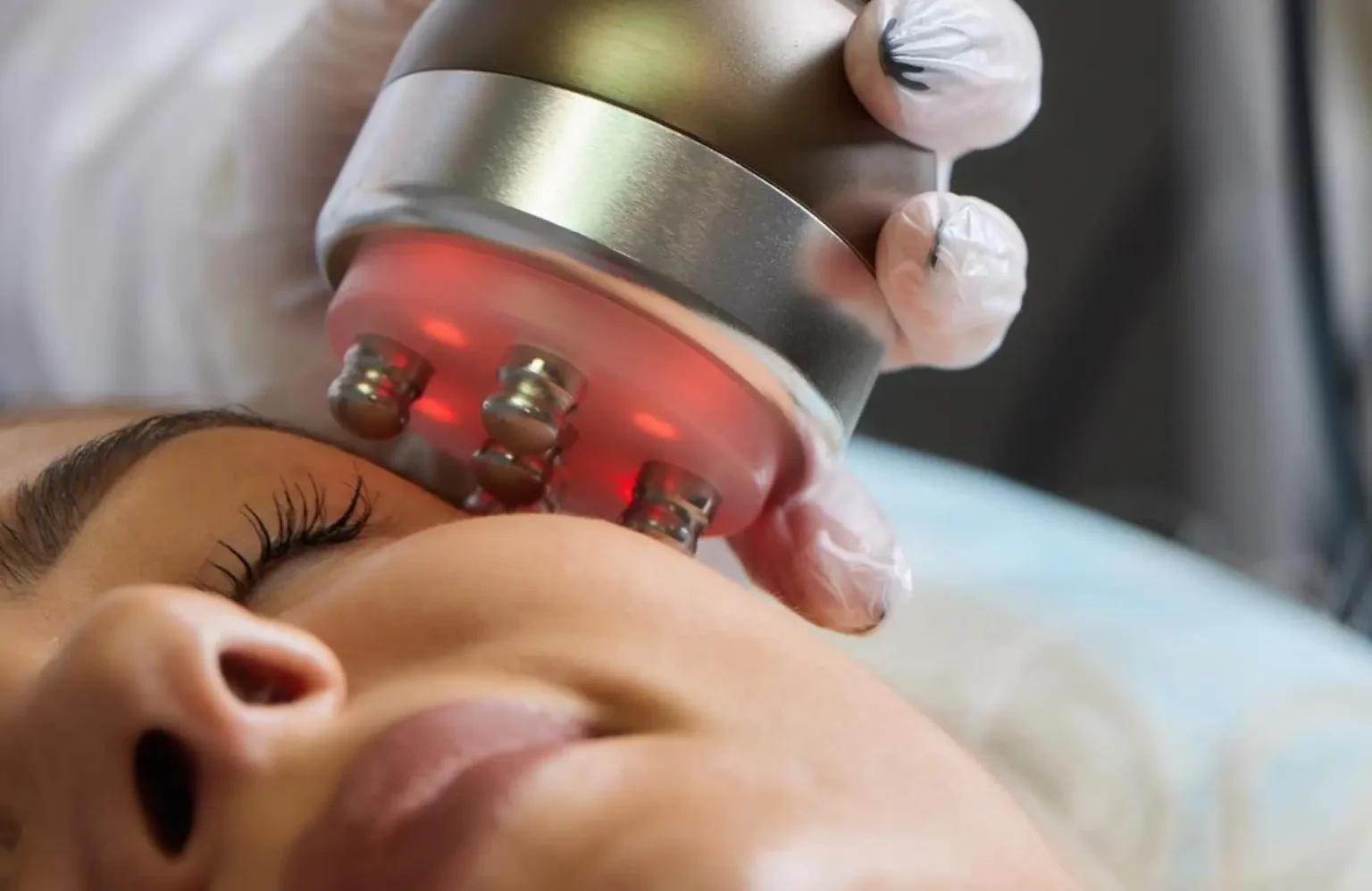 Lydia Esthetics Embassy A person receives a facial treatment with a handheld device emitting red light, operated by a gloved hand. New York