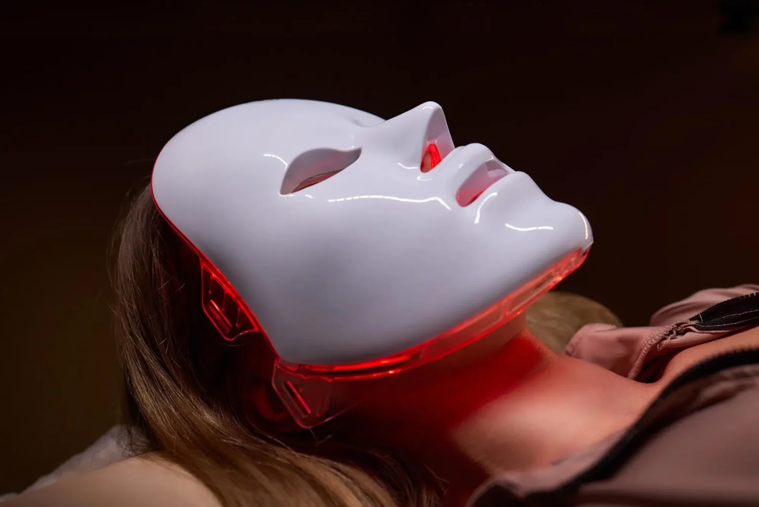 Lydia Esthetics Embassy A person lies down wearing a white LED light therapy mask that emits a red glow around the chin and jawline. New York