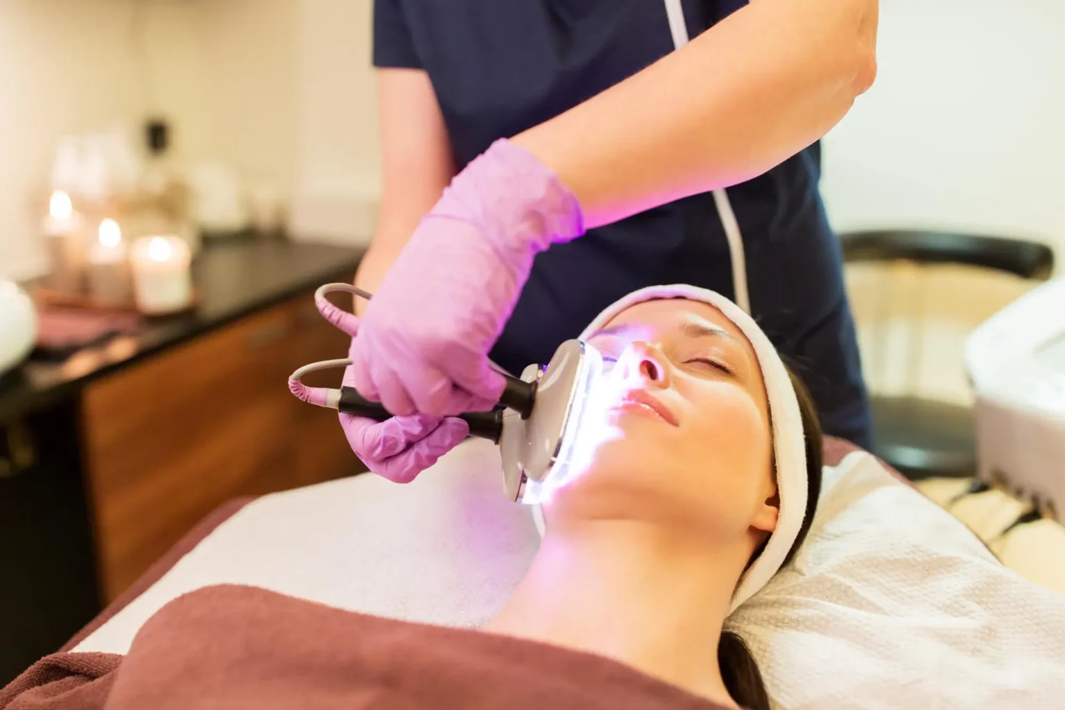 Lydia Esthetics Embassy A person receives a facial treatment with a handheld light therapy device by a professional wearing gloves in a spa setting. New York