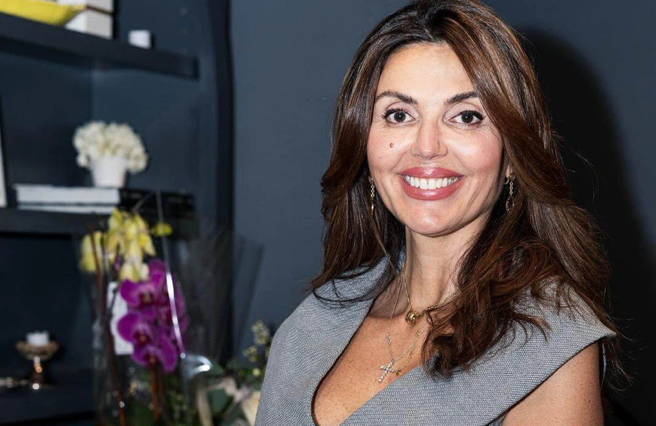 Lydia Esthetics Embassy A woman with long brown hair and a gray dress smiles at the camera; a shelf with flowers and books is in the background. New York