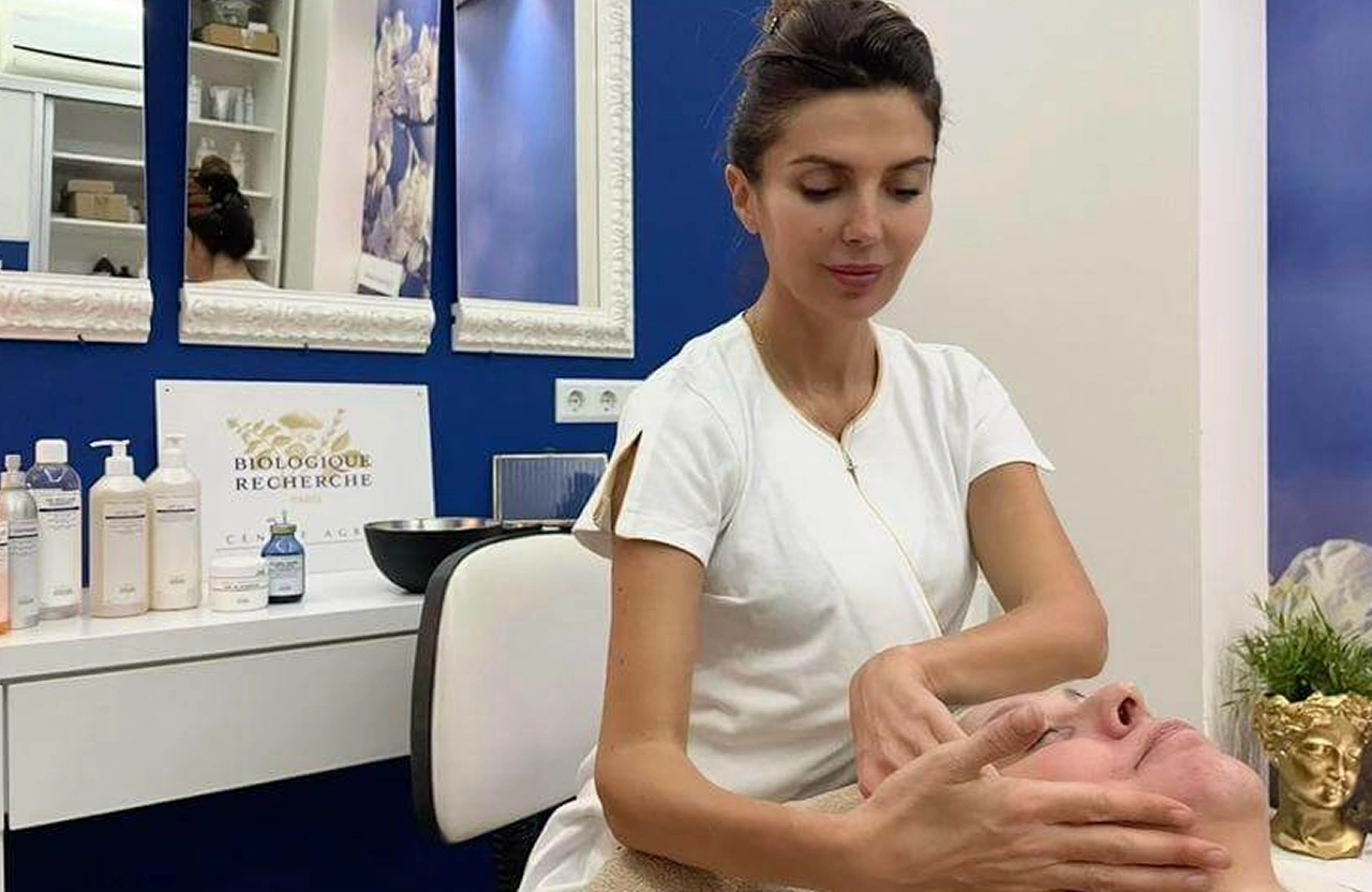 Lydia Esthetics Embassy A woman in a white uniform gives a facial massage to a client in a skincare treatment room with blue and white decor. New York