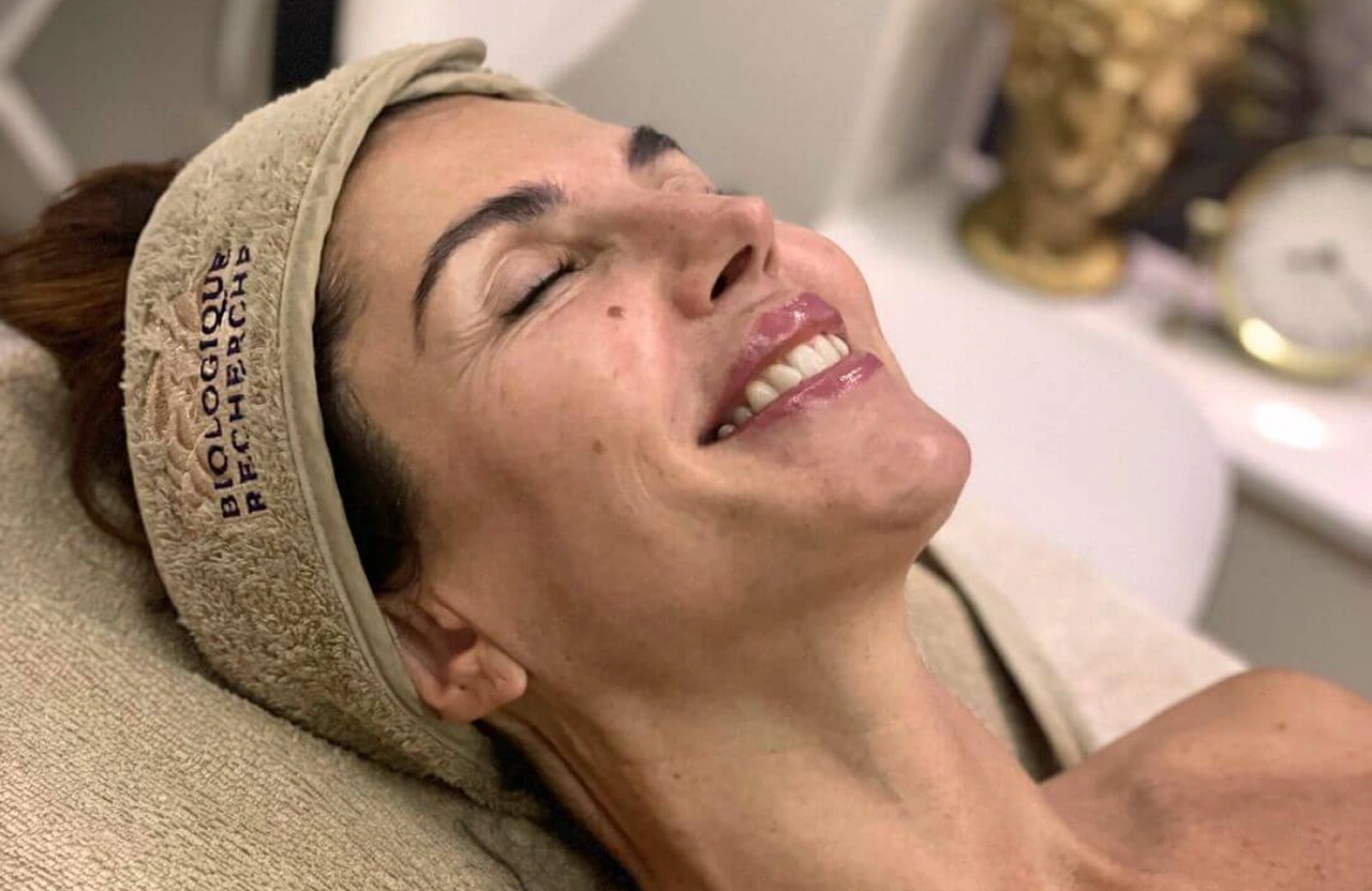 Lydia Esthetics Embassy A woman with a headband lies back and smiles during a facial treatment in a spa setting. New York
