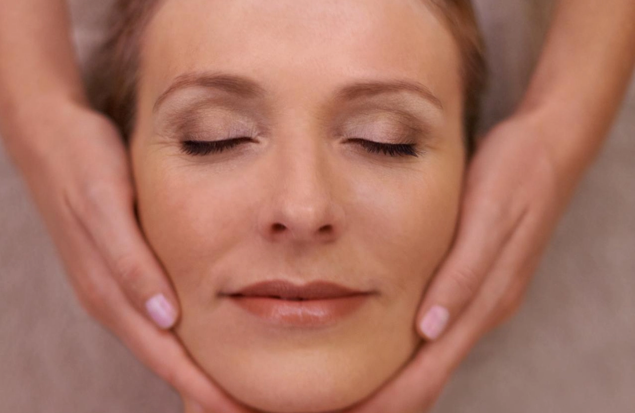 Lydia Esthetics Embassy A person with closed eyes receives a facial massage, with hands gently holding their face. New York